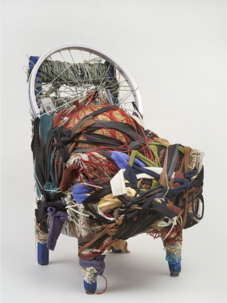 A sculptural artwork consisting of various textiles and materials tightly wrapped around a chair-like structure, creating an intricate, cocoon-like form.